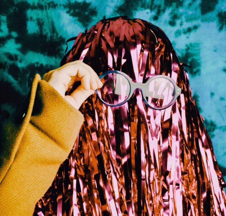 Woman posing for a school photo in a pom pom wig and glasses